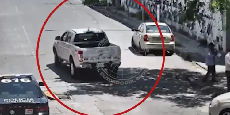 Surveillance Frame of a White Pickup Truck in the Middle of a Street, Circled in Red, with a Beige Car Nearby and Bystanders on the Sidewalk. - Nuevo León Primero