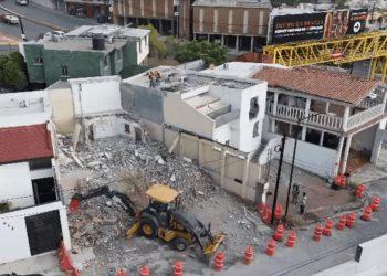a Demolition Site in a Residential Area: Rubble, a Small Backhoe on Debris, and Orange Traffic Cones by the Intact Surrounding Buildings. - Nuevo León Primero