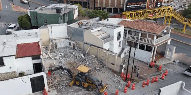 a Demolition Site in a Residential Area: Rubble, a Small Backhoe on Debris, and Orange Traffic Cones by the Intact Surrounding Buildings. - Nuevo León Primero