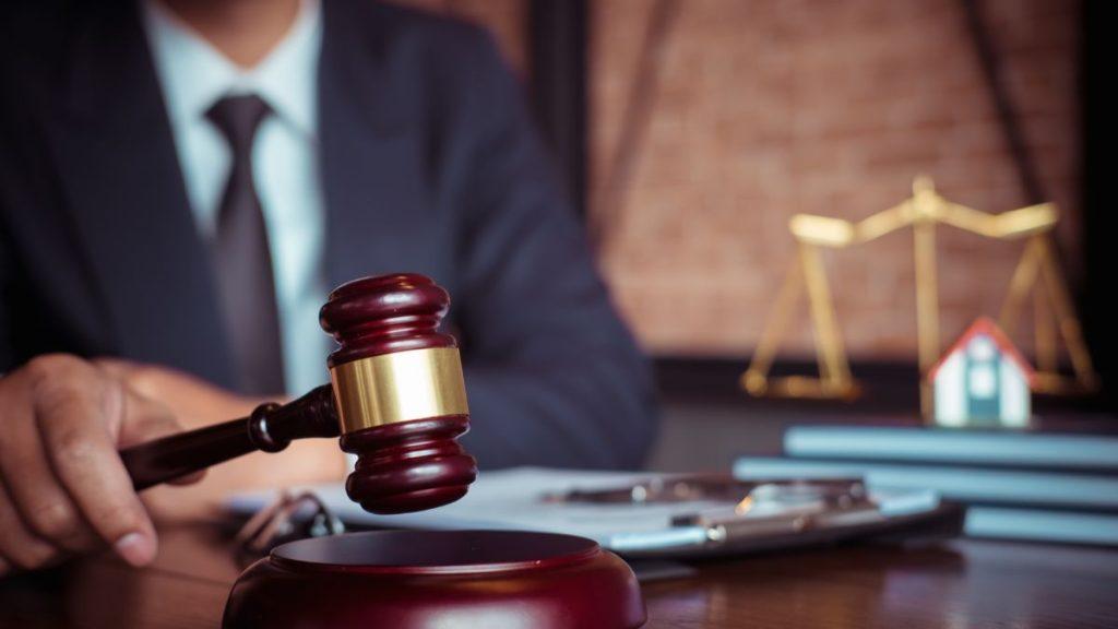Tramite-para-comprar-una-casa-usada - Nuevo León Primero Gavel on a Wooden Desk with Legal Papers; Blurred Scales of Justice and a Small House Model in the Background, Signaling Law and Real Estate Justice. - Nuevo León Primero