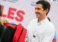 Smiling Man in a White Shirt Hands a Red Backpack to a Person at a Public Event with Large Red Letters in the Background. - Nuevo León Primero