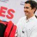 Marcelo Segovia En La Entrega De útiles útiles - Nuevo León Primero Smiling Man in a White Shirt Hands a Red Backpack to a Person at a Public Event with Large Red Letters in the Background. - Nuevo León Primero