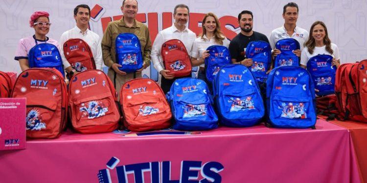 Group of Eight Adults Standing Behind a Table with Red and Blue Mty Backpacks at a Back-to-school Event. the Banner Shows Education Ministry Logos in Spanish Context. - Nuevo León Primero
