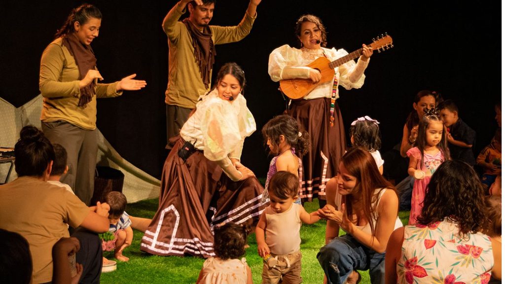 Teatro Para Bebés - Nuevo León Primero Performers in Matching Costumes Dance and Play Guitar on Stage While Children and Adults Watch Nearby. - Nuevo León Primero