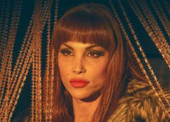 Portrait of a Woman with Red Hair and Bold Makeup, Wearing a Fur Collar, Gazing at the Camera with Gold String Lights in the Background. - Nuevo León Primero