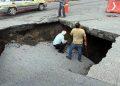 Large Sinkhole in a Paved Road with Two Workers Inspecting the Edge, Caution Tape, and Traffic Cones Nearby. - Nuevo León Primero