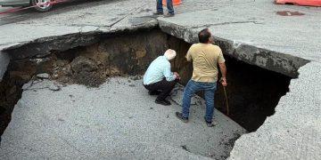 Large Sinkhole in a Paved Road with Two Workers Inspecting the Edge, Caution Tape, and Traffic Cones Nearby. - Nuevo León Primero