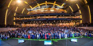 Huge Group of People in Formal Attire Posing on a Multi-tiered Stage in a Modern Auditorium; 'juntos' Signs Visible at Front. - Nuevo León Primero