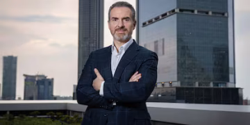Confident Businessman in a Dark Suit Stands with Arms Crossed on a Rooftop, with a City Skyline in the Background. - Nuevo León Primero