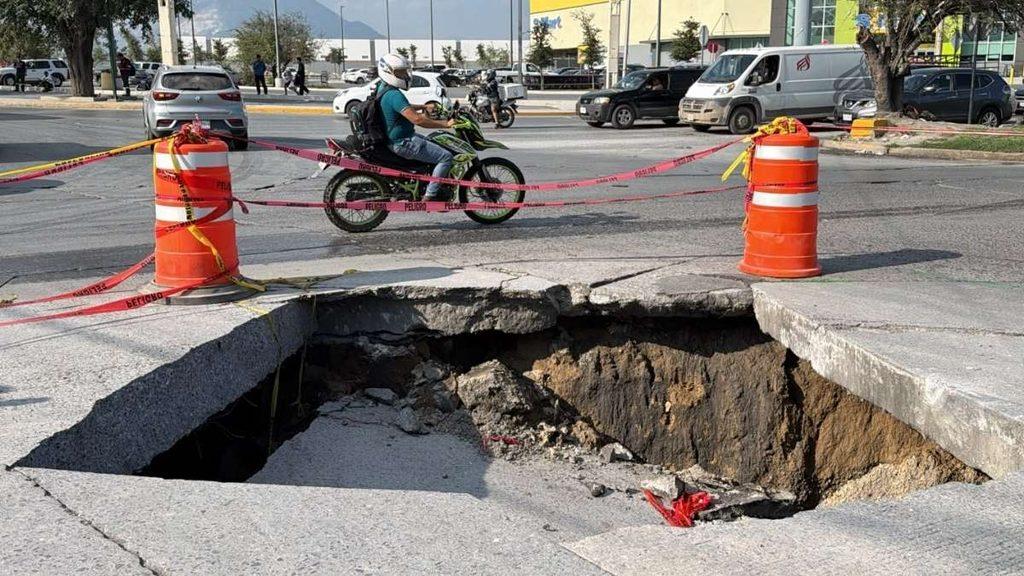 Autoridades-municipales-acordonaron-interseccion-camino - Nuevo León Primero Sinkhole Opens in City Street, Surrounded by Orange Traffic Barrels and Caution Tape As a Motorcyclist Rides Past. - Nuevo León Primero